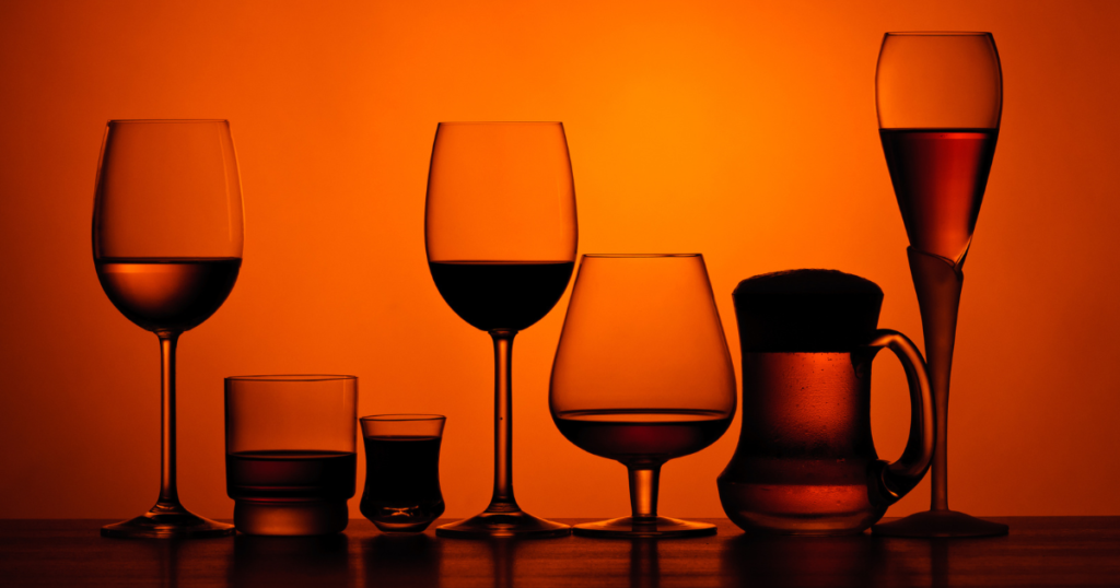 Different alcoholic drinks lined up against a glowing orange backdrop.