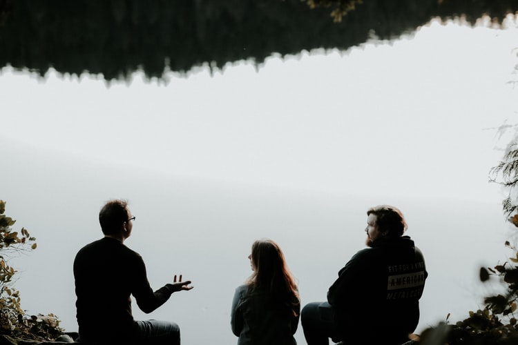 Three people sitting by a lake talking about amends they want to make regarding their addiction recovery