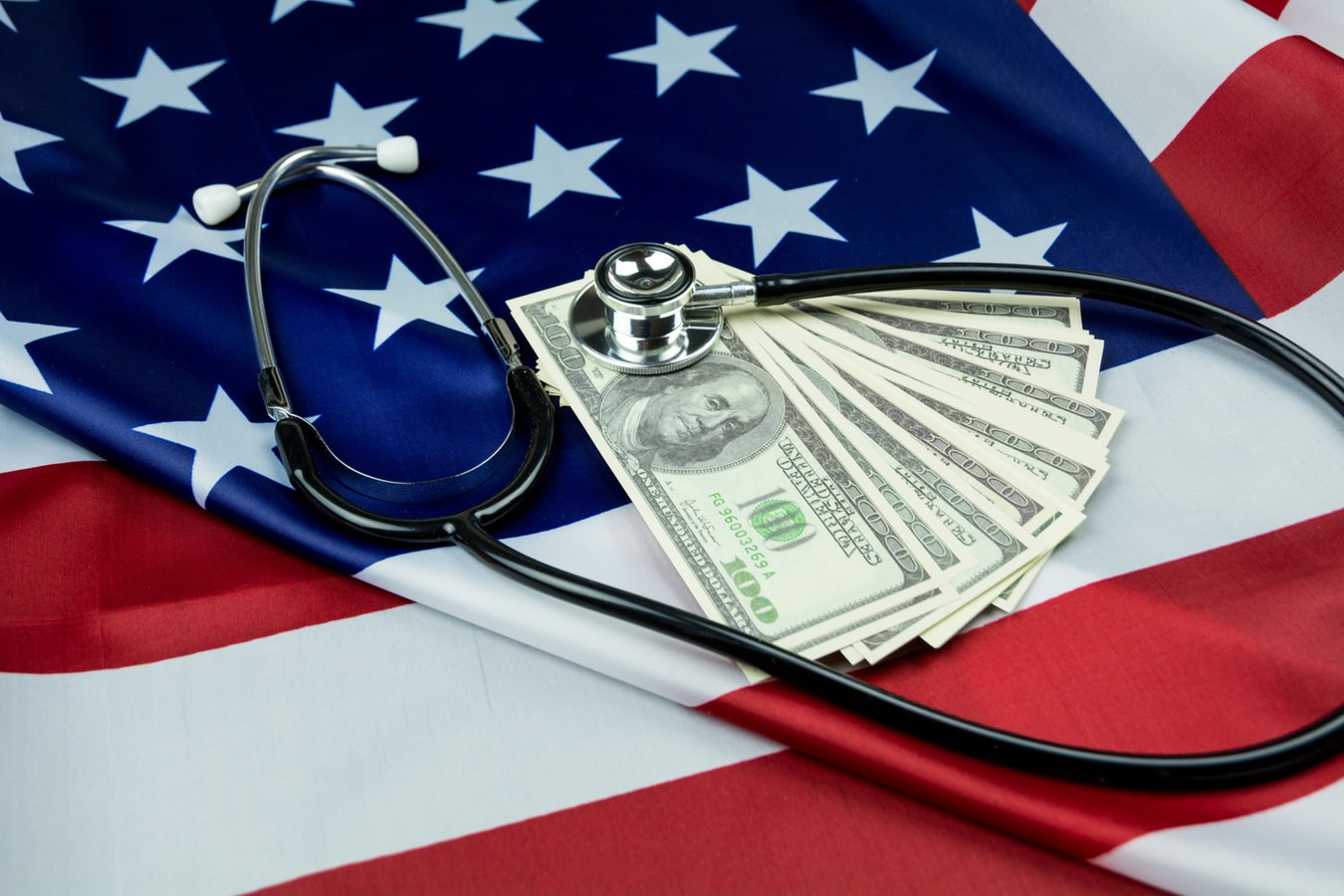 A stethoscope on top of money and an american flag. Excessive drinking can lead to extreme healthcare costs