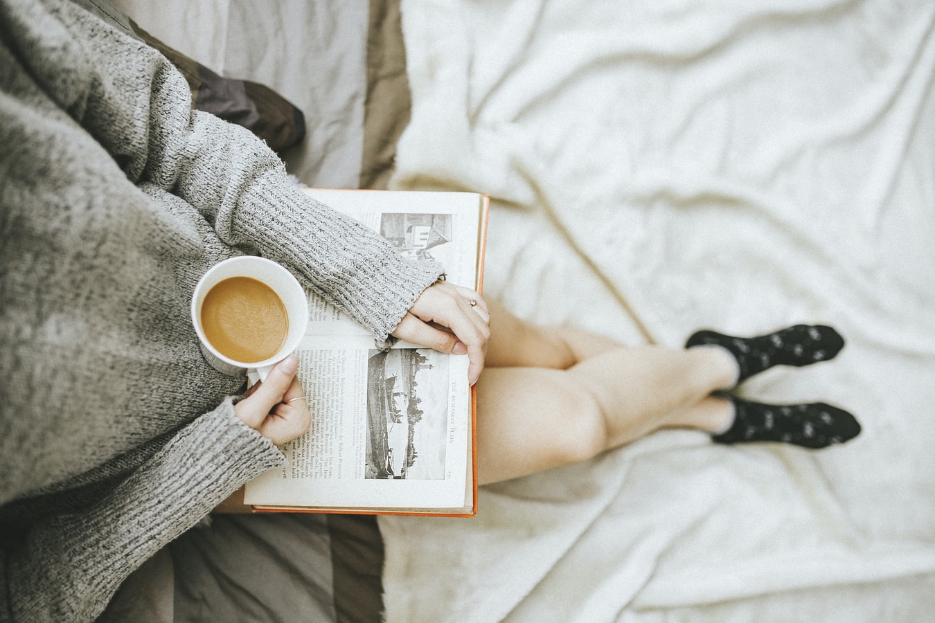 An individual relaxing while drinking coffee and reading a book.
