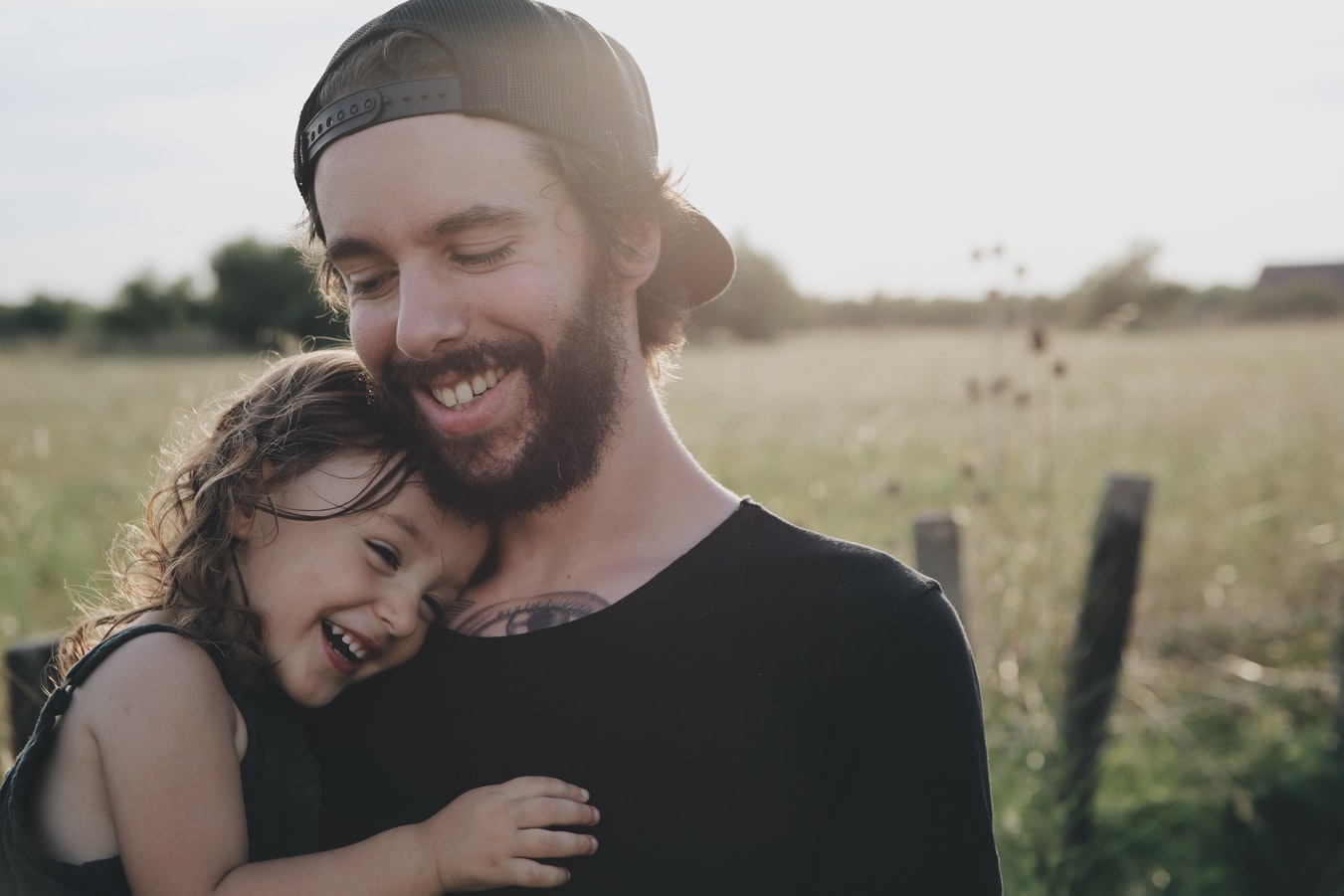 A young man smiling with his daughter in a grass field