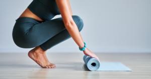 Woman rolling up a yoga mat on a tile floor.