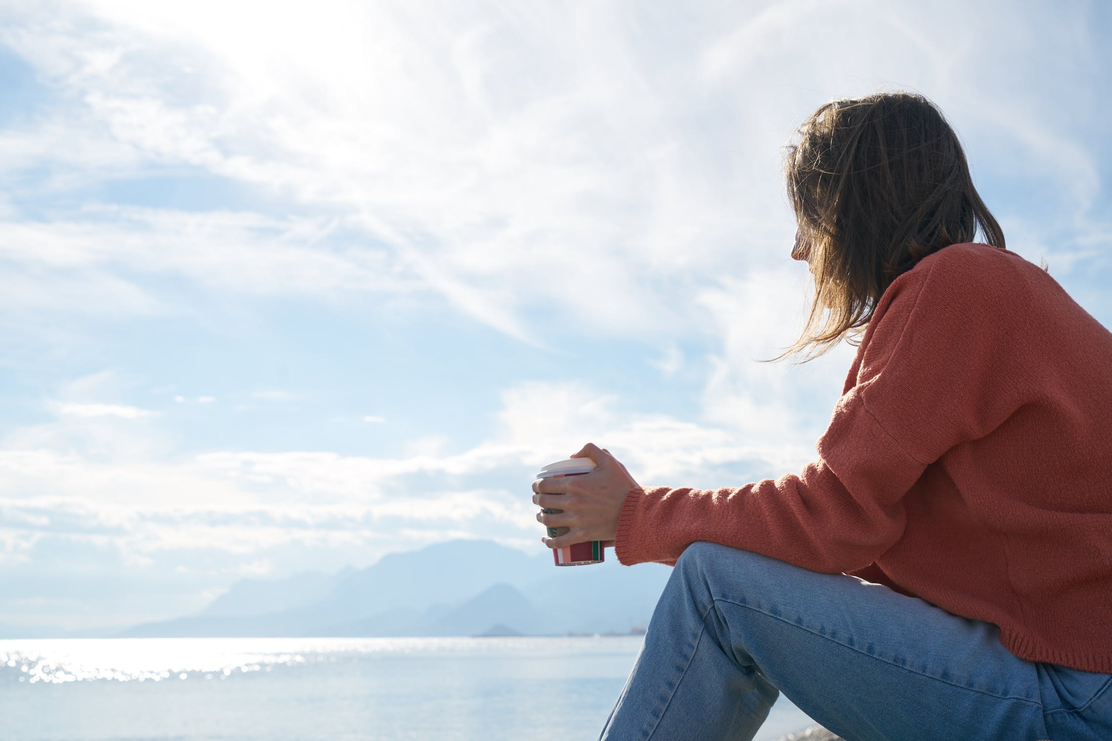 A woman holding coffee and overlooking the water thinking about how to prevent a relapse on alcohol