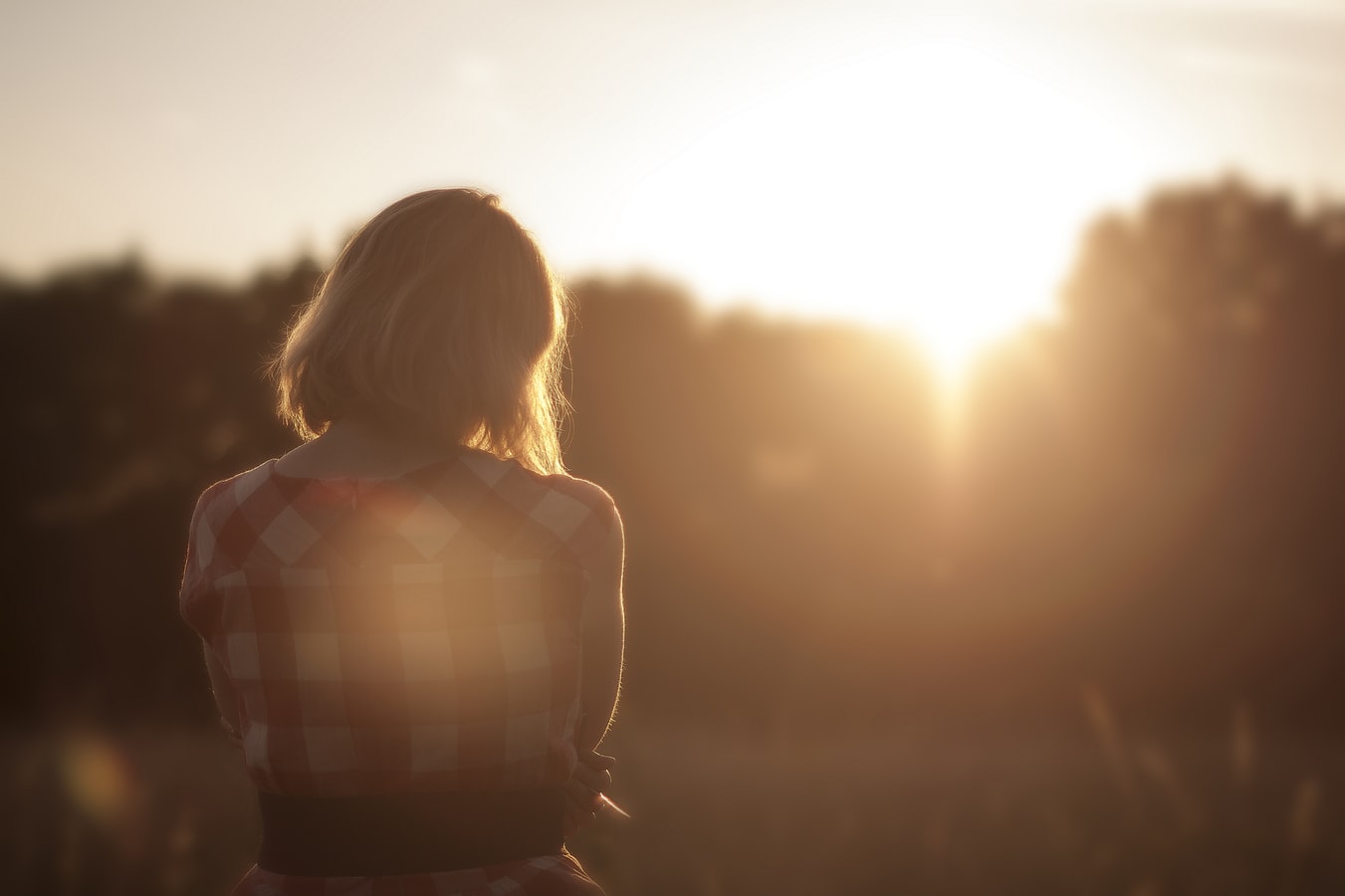 A woman standing watching the sunrise wondering if she should attend an alcohol rehab program