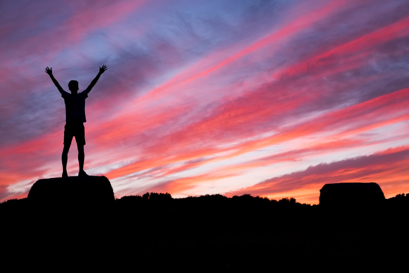 A man standing on a rock at sunset with his hands in the air because he is happy that a SMART Recovery program is working