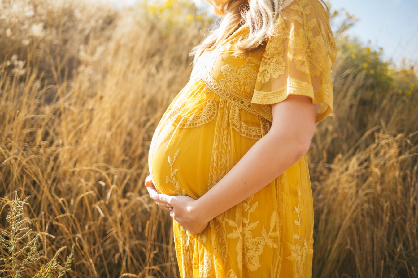 A pregnant woman holding her belly in a field outdoors