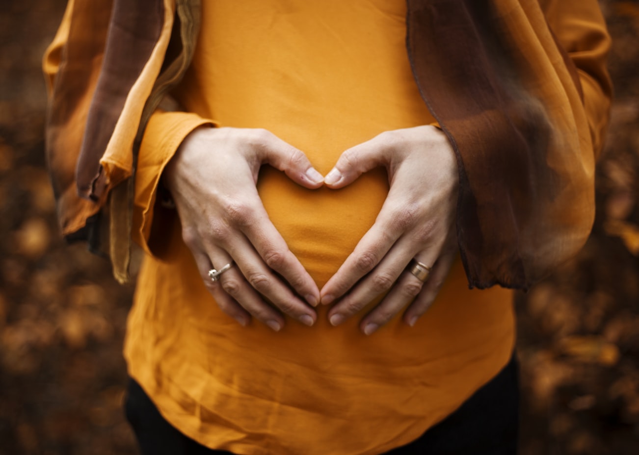 A woman holding her hands in a heart shape over her belly.
