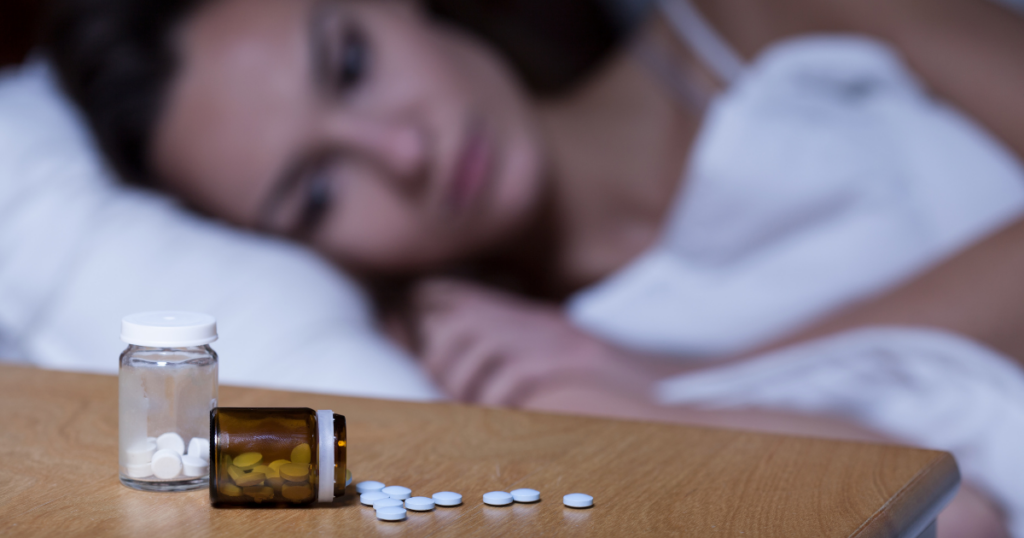 A woman laying in bed looks at pills in a bottle. 