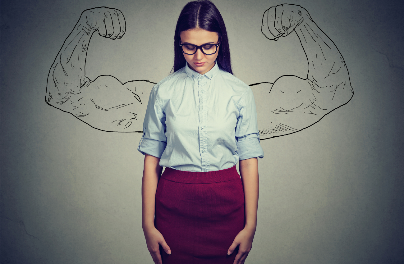 A young woman wearing glasses and a skirt stands in front of an illustration of strong, muscle bound arms.
