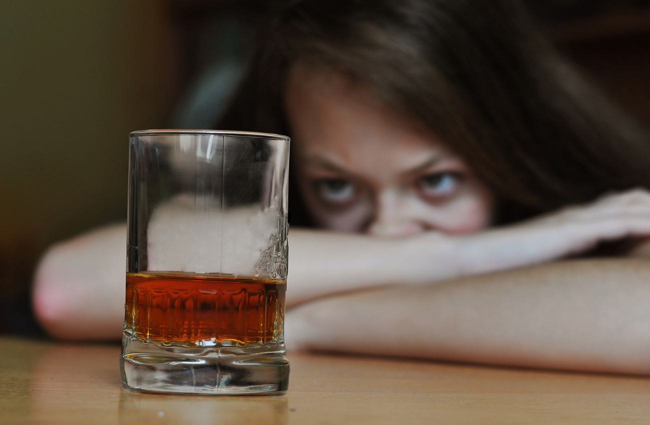 A woman stares at a glass of brown alcohol, wondering if she should drink or not.