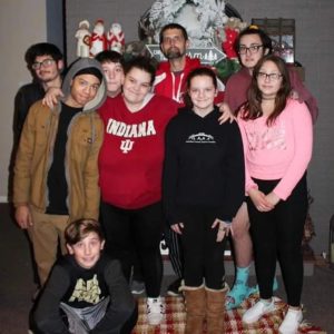 Dustin and eight children in hoodies and coats for a family photo at Christmas time in front of the fireplace