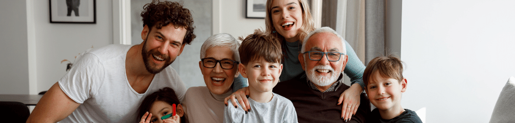 Smiling grandparents seated on the couch with grandchildren on their laps and parents leaning over their shoulders from behind the couch. A success story from Landmark Recovery's substance abuse treatment that started with an intervention.