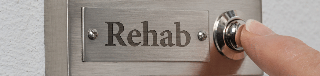 A metal plate with a crooked, smaller plate screwed onto it and the word "Rehab" on it. A finger pressing the button next to it to buzz the residential treatment center.