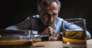 A disheveled alcoholic staring at a bottle and glass of whiskey at the precipice from which a fall could land him at rock bottom just as quickly as a meth user not seeking meth addiction treatment.