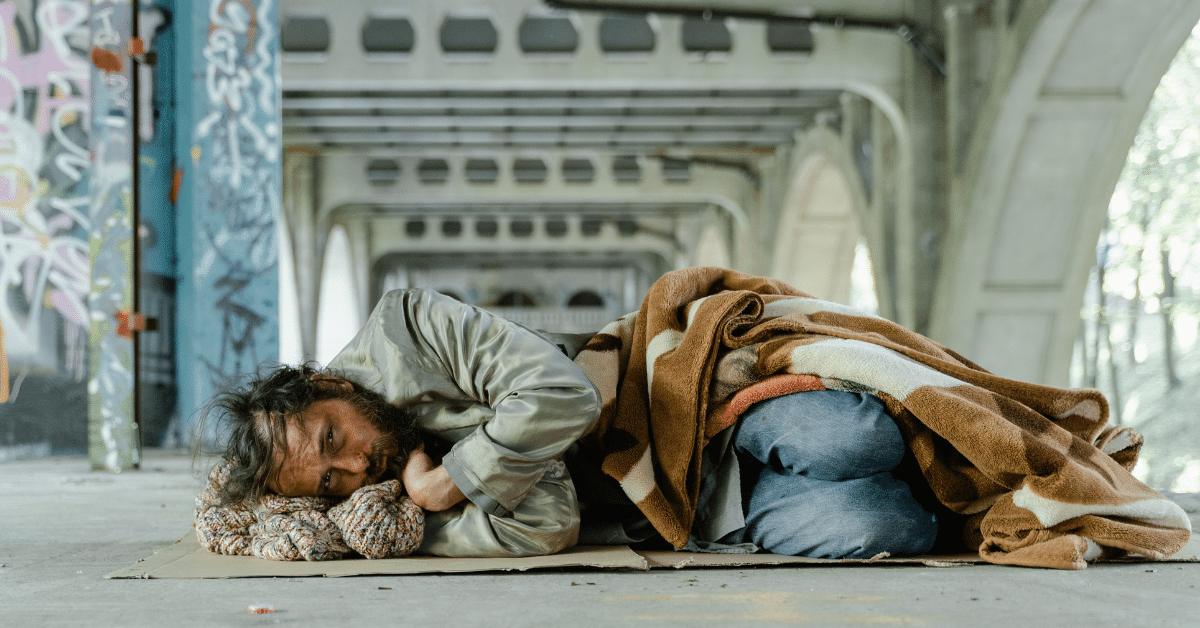 A man who has hit rock bottom rather than seeking meth addiction treatment, sleeping under a bridge on a flattened, cardboard box.
