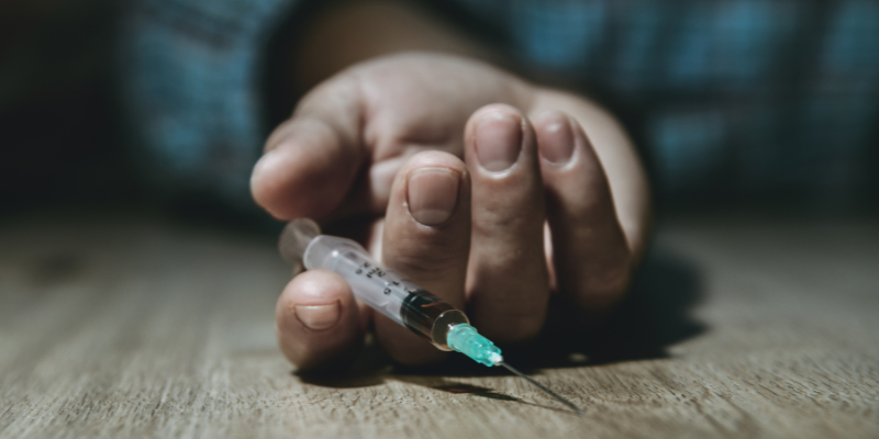 A person lays on the floor holding a syringe after a drug overdose