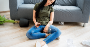 A woman sits in the floor at home falling asleep while drinking. She would be better off at a halfway house or better still at a sober living house after addiction treatment at Landmark Recovery of Knoxville.