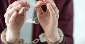 Man with handcuffs around his wrists holds up a tiny baggy of pills. When it comes to drug trafficking Attorney Generals in Tennessee are focused on operations from Michigan entering the state.