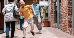 A child with ADHD runs through a corridor of an outdoor mall with his father chasing him as he darts around a passer-by. The boy has ADHD and addiction tendencies.