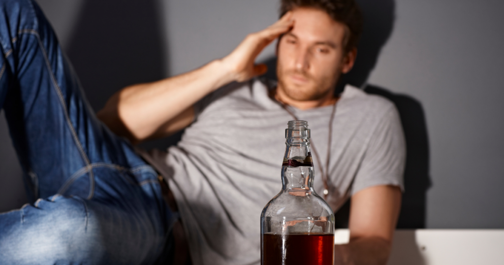 a man with a substance use disorder stares at an alcohol bottle. He realizes his substance abuse has led to mental health issues