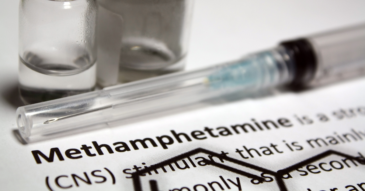 a syringe and liquid bottle sit on top of a paper that says methamphetamine, or meth