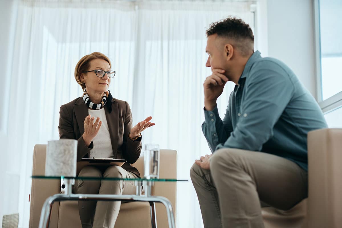 female therapist talking to a young man in an office setting about overcoming stigma and the importance of MAT in recovery.